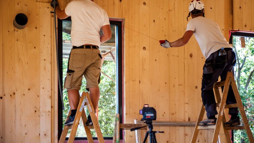 Two Construction workers with ladder at construction site in wooden house.