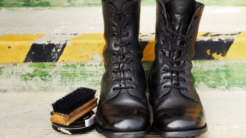 A pair of polished black leather lace-up boots next to a brush and tin of shoe polish. 