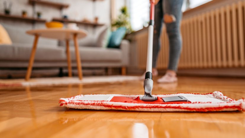 A woman using a mop to clean a wooden floor.