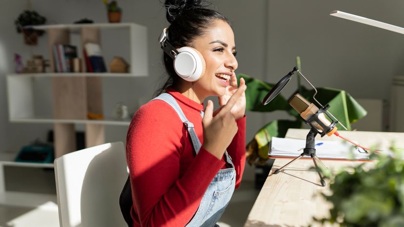 A woman at home speaking into a microphone while wearing headphones. 