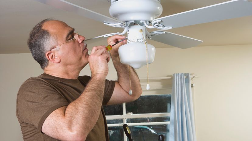 A man using a screwdriver to fix a ceiling fan. 