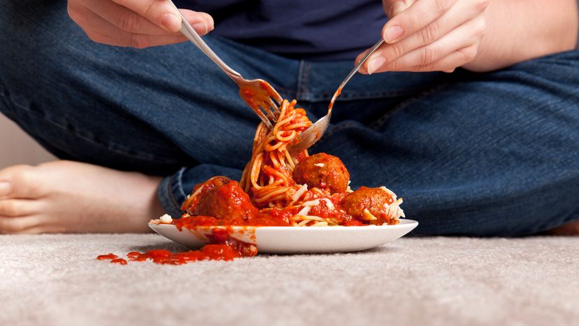 A man eating spaghetti while the sauce spills on the carpet.