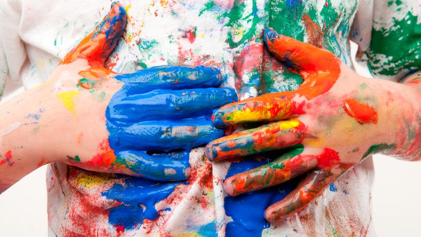 A child with watercolor paint on his hands and shirt. 