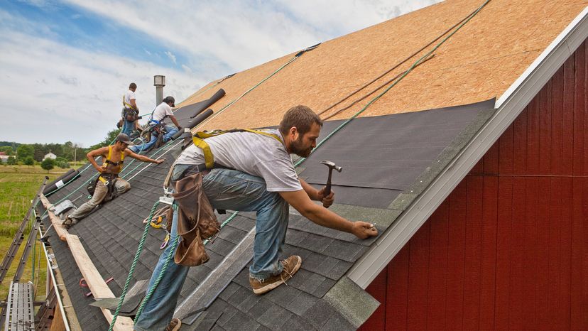 Construction workers hammering shingles onto a roof.