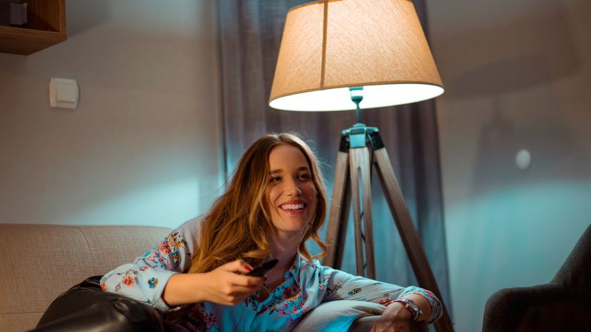 Young woman watching tv at night with a lamp beside the couch. 