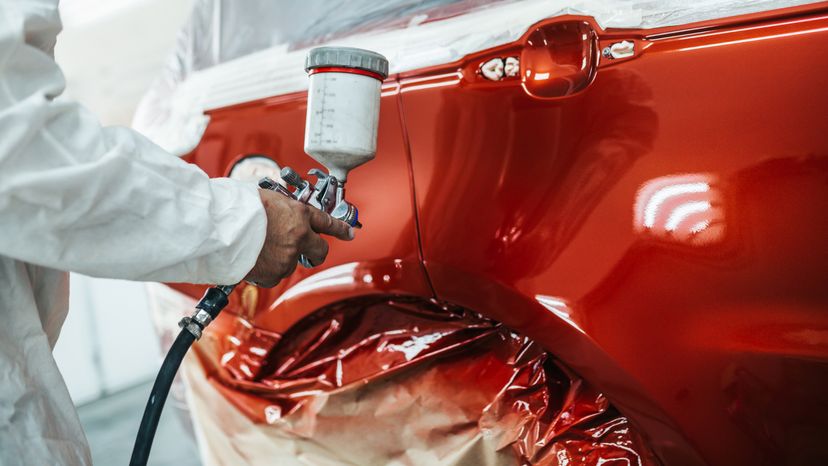 A Man with protective clothe painting a car using spray compressor.