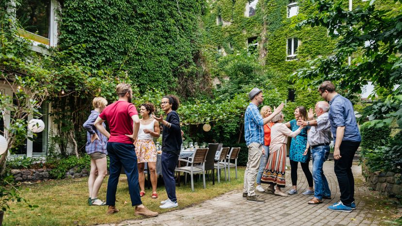 A group of men and women standing in a backyard having discussions. 