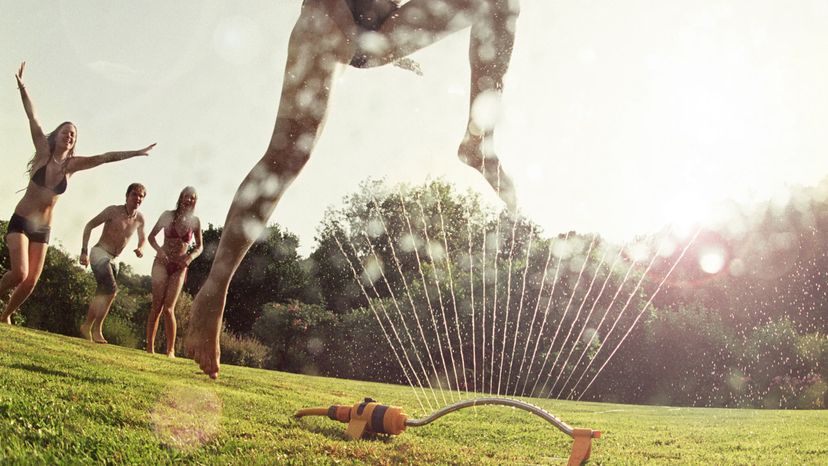 Young women in bikinis playing over a sprinkler. 