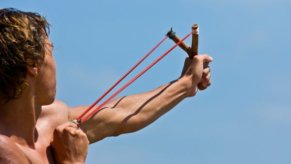 A young man fires a stone from a slingshot.