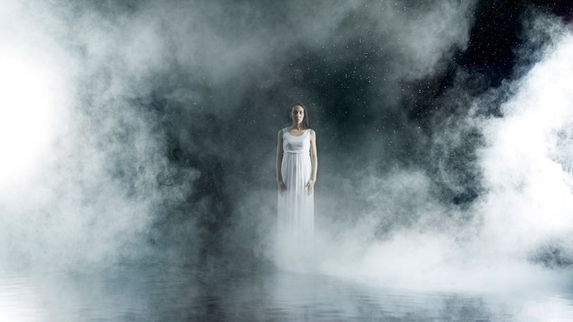 A woman standing on a stage surrounded with fog. 