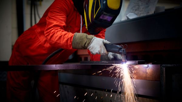 Close up image of a man using a plasma cutter in a steel fabrication factory.