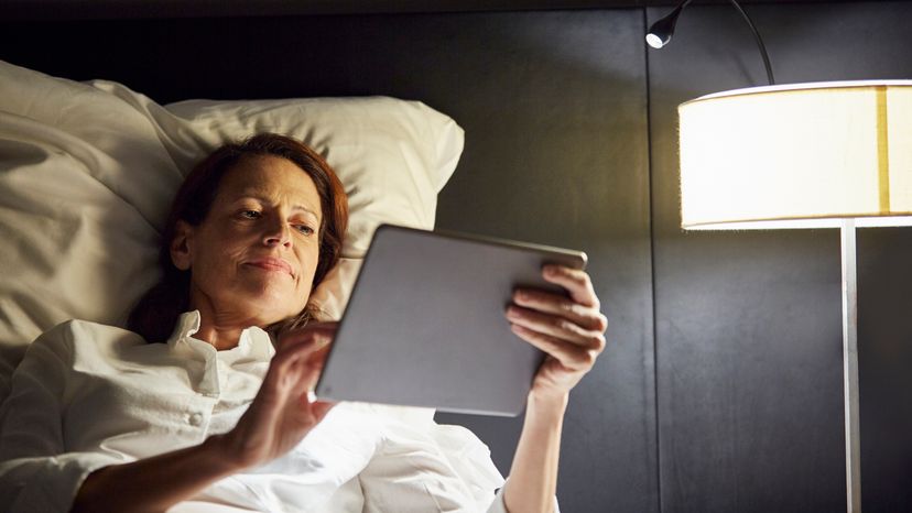 A woman smiling while using her phone in bed, with a touch lamp beside her. 