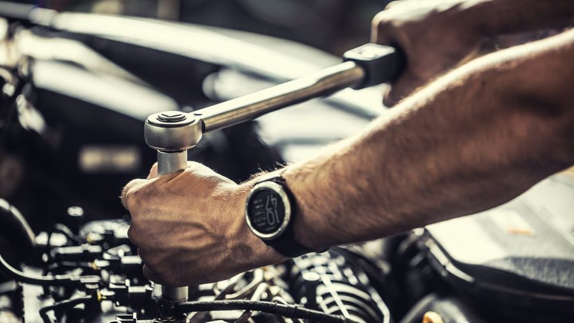 A mechanic working on a broken car engine with a torque wrench. 