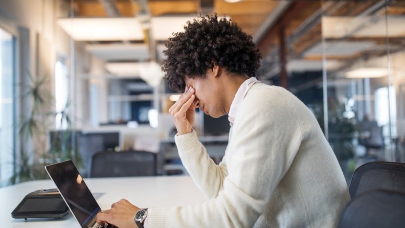 A young woman working in her office, looking tired and stressed. 