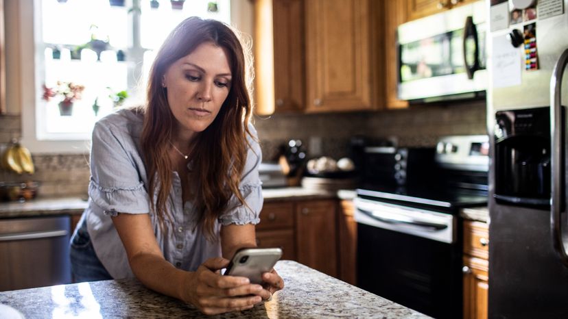 Woman using mobile device in kitchen at home.