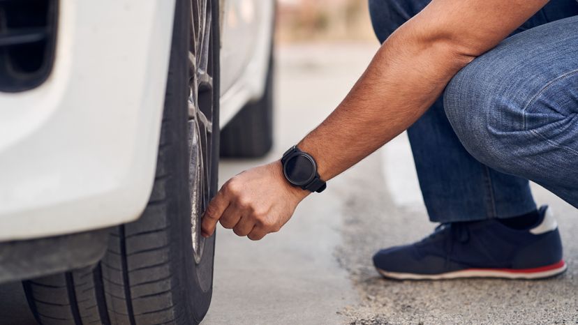 A close up image of a man checking his cars tires. 
