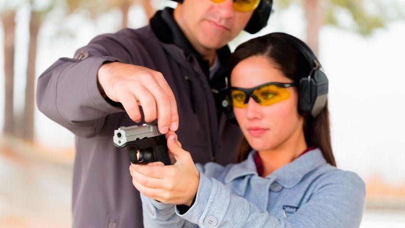 A young woman with her instructor practicing how to shoot a gun at a shooting range. 