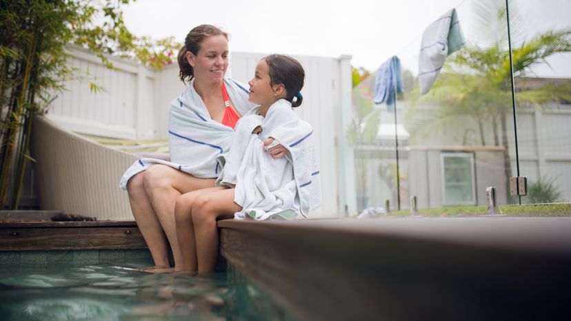 A mom using a towel to cover her daughter by the pool. 