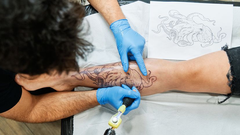 A tattoo artist tattooing the image of an octopus on a persons leg. 