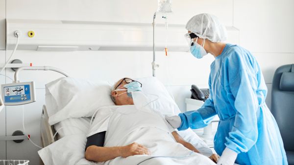 A female doctor wearing protective suit while attending to a senior patient. 