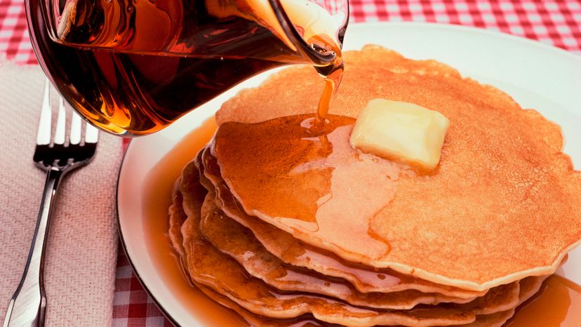 Maple syrup being poured on a heap of pancakes. 