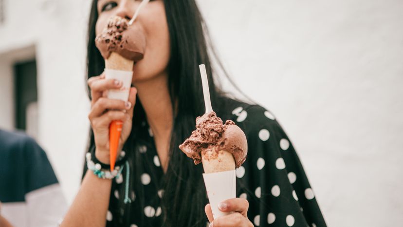 A young lady licking a chocolate ice cream while holding another.