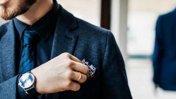 A close up picture of a man putting a handkerchief in his breast pocket. 