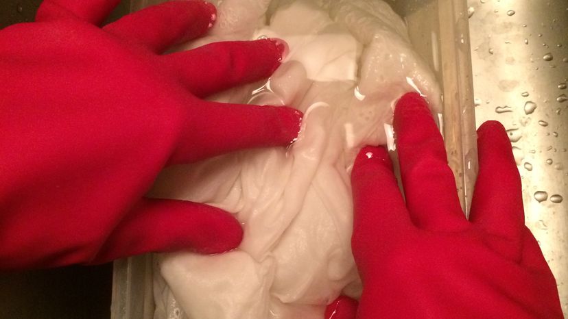 A hand in red gloves, bleaching a fabric. 
