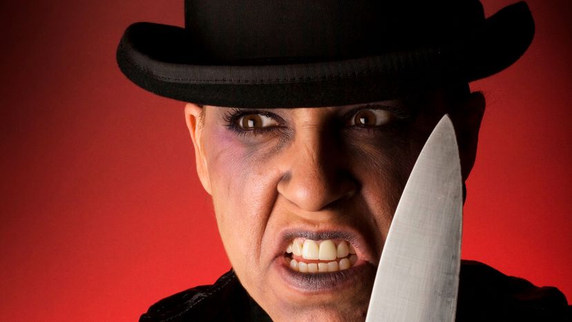 A man wearing a black hat and holding a knife. 