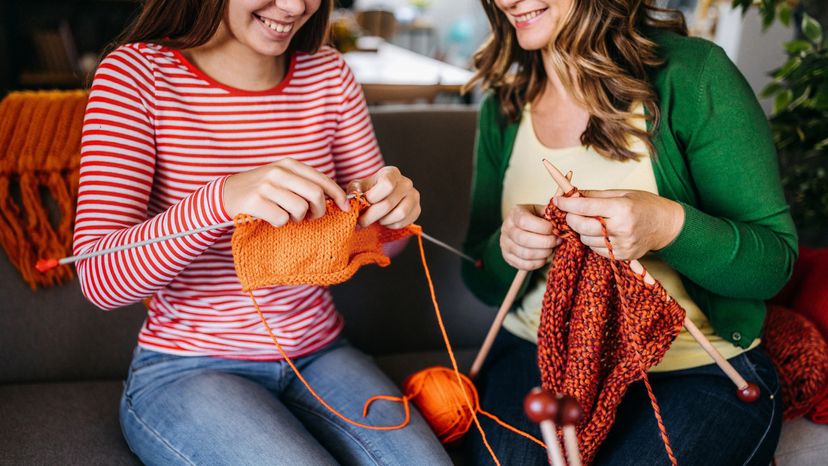 A mom and daughter happily knitting together.
