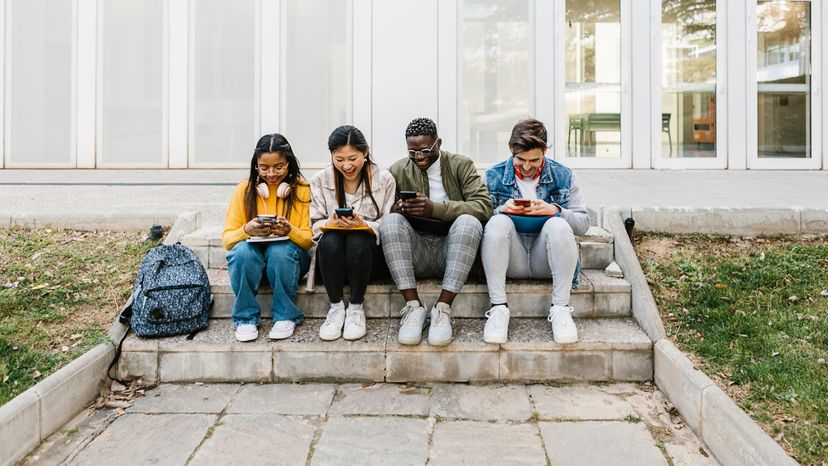 Four young students making use of their cell phones.