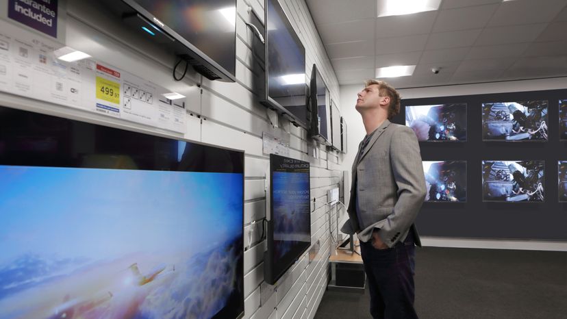 A man standing in a store while looking at a plasma tv screen. 