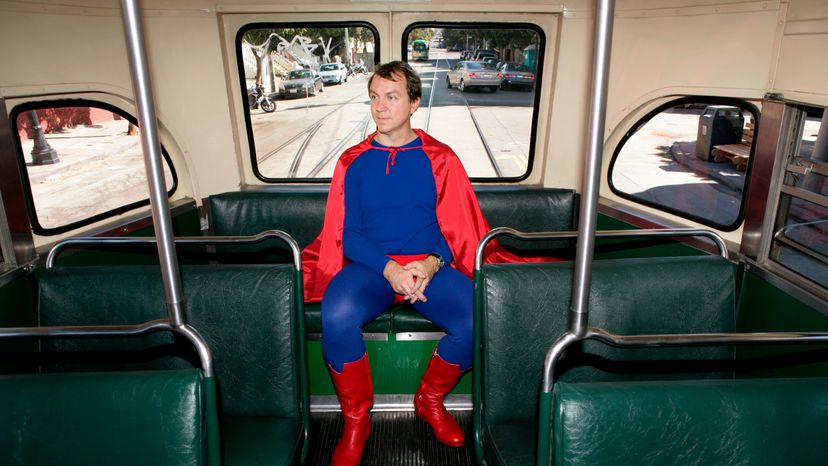 A man in a superhero costumer sitting at the back of a bus.