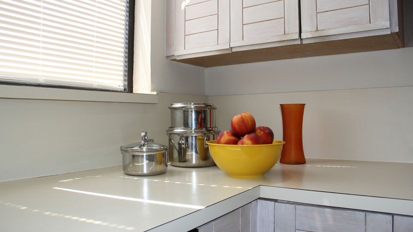 A kitchen countertop with a bowl of apples, pots and a vase. 