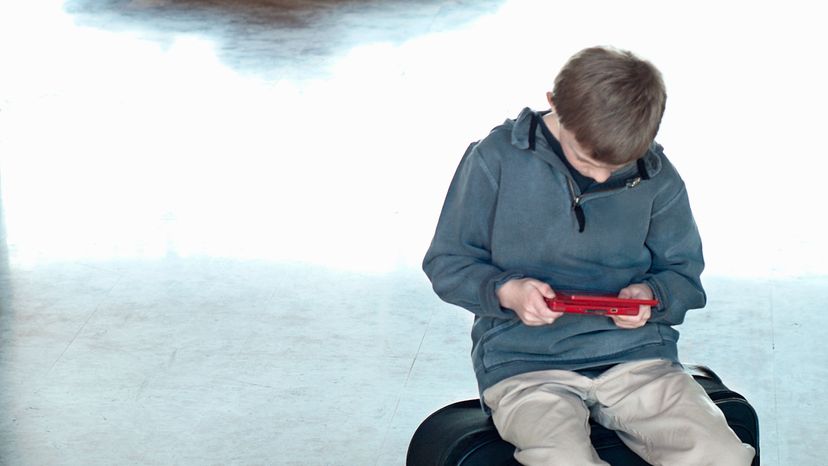 A boy playing with his Nintendo in an airport lounge. 