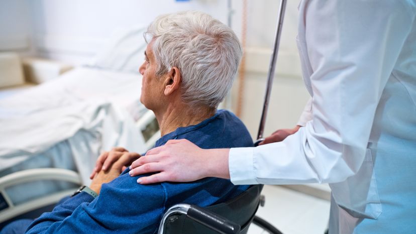 An elderly man being pushed in a wheelchair by a nurse. 