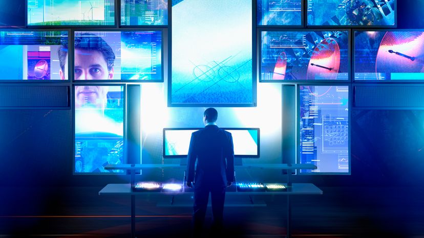 A man standing in front of large computer monitors. 