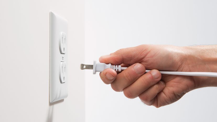 A mans hand plugging an electrical plug into an outlet. 