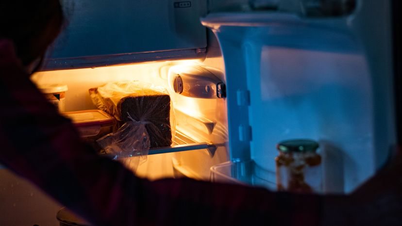 A woman looking at the inside of a fridge at night. 