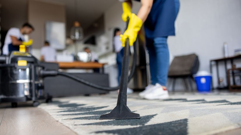A close up of a professional cleaner using a vacuum cleaner on a carpet. 