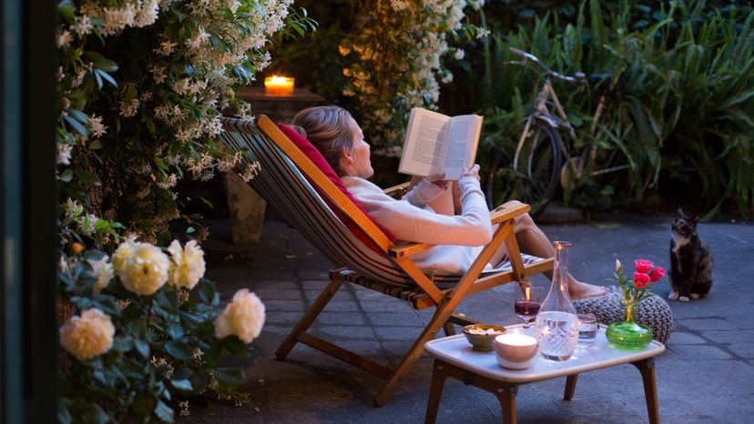 A woman reading a book in her backyard.