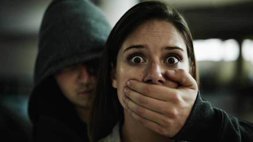 A man holding his hand over a scared woman's mouth. 