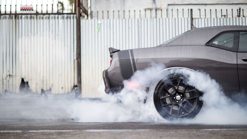 A car rolling it tires on a pavement causing smoke to rise. 