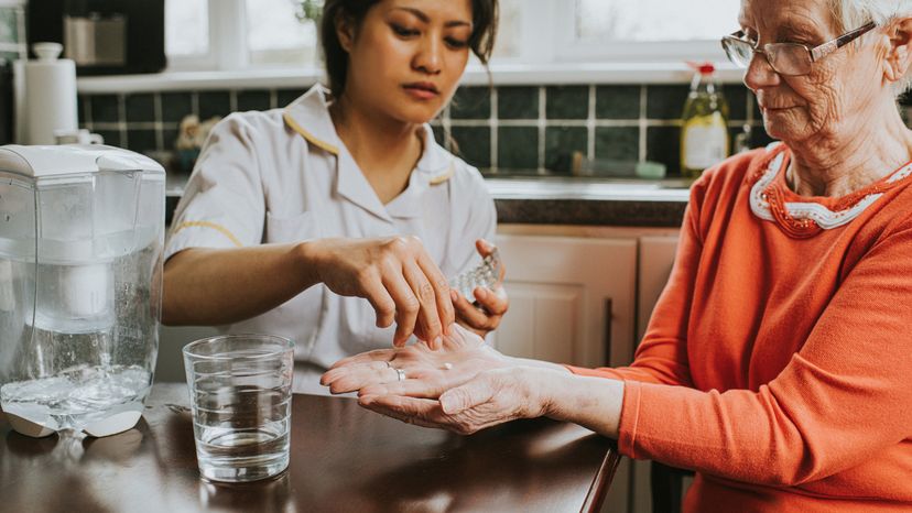 A female caregiver giving an elderly woman her pills. 