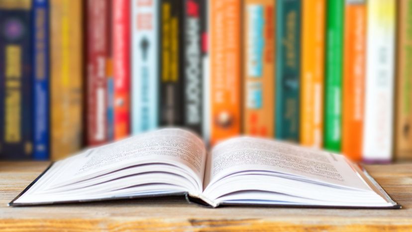 An open book in front of a bookshelf filled with books. 