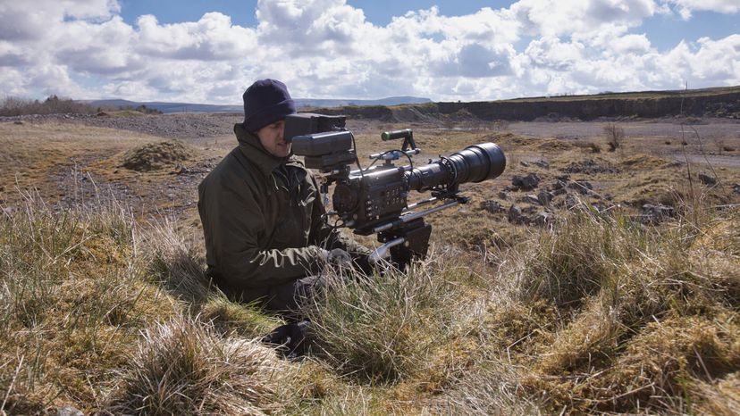 A man with his camera, filming in the woods. 