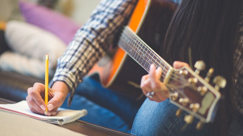 A lady writing while holding a guitar. 