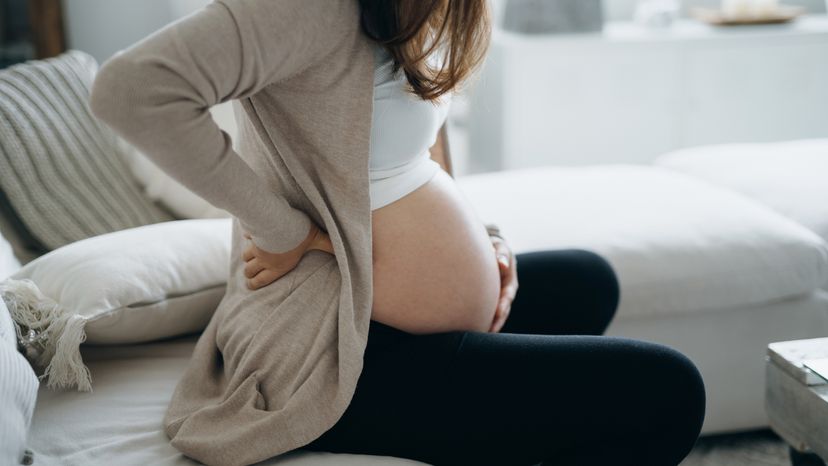 A pregnant woman holding her waist while sitting. 