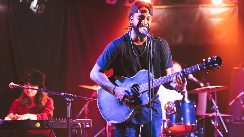 A black male guitarists playing an acoustic guitar on stage. 