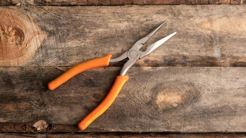 A needle nose plier with orange handles on a wood background. 